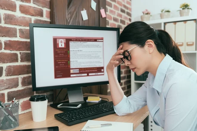 Женщина сидит перед компьютером, зараженным вирусом-шифровальщиком